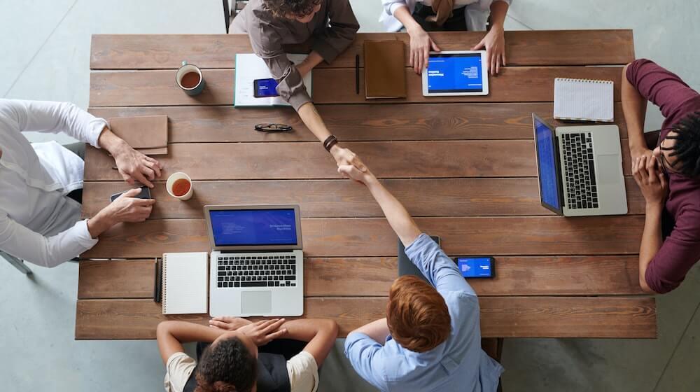 People sitting at table with computers and shaking hands