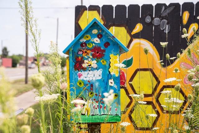 A colorfully painted beehive in front of a fence with a black and yellow honeycomb design