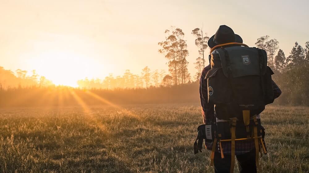 Person backpacking through field and sunset