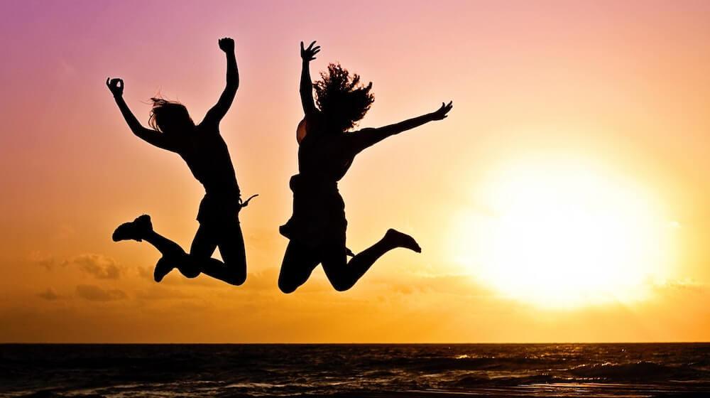 Two people jumping on a beach at sunset
