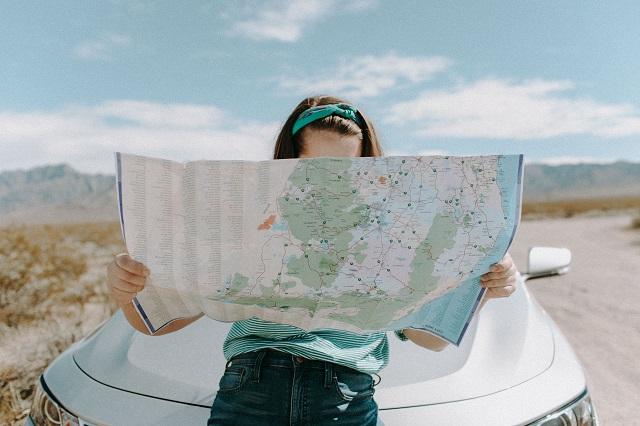Woman sitting on a car hood studying a map