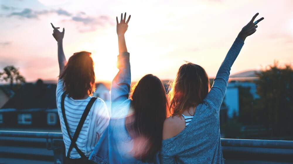 Three people facing a sunset