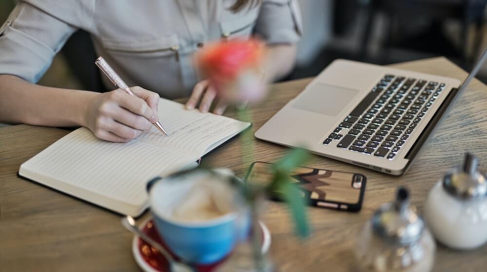 Person taking notes in front of laptop