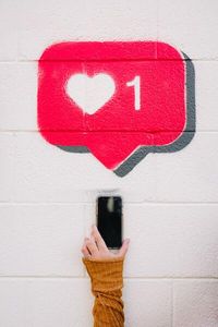 Social media heart symbol painted above someone's arm holding a cell phone