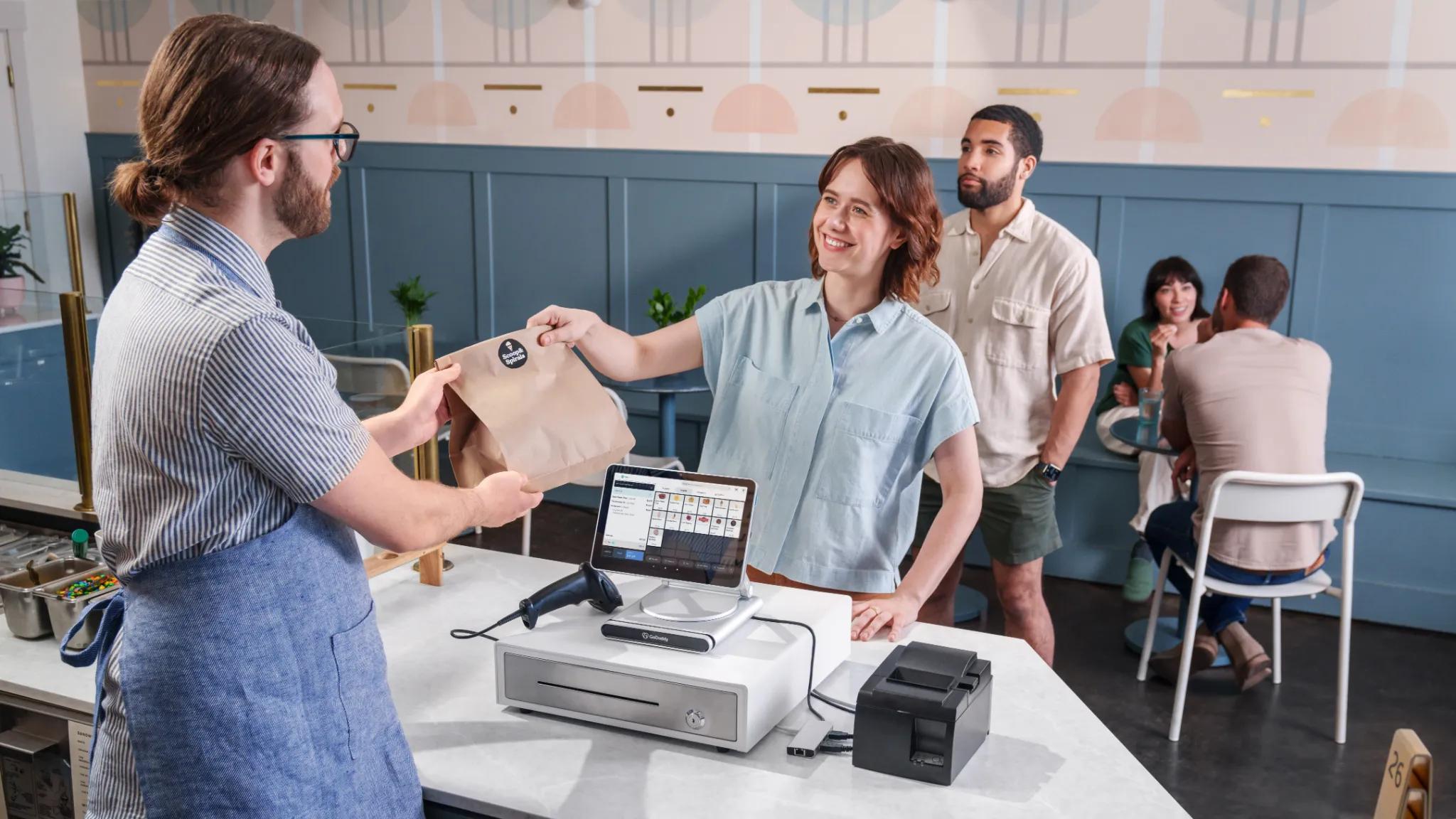 Cafe worker handing mobile order to customer after completing their purchase.