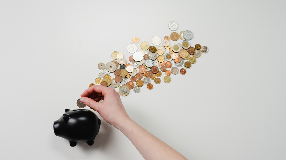Person placing money into piggy bank with coins scattered behind