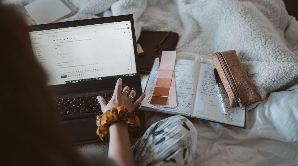 Woman sitting on bed while composing an email on a laptop