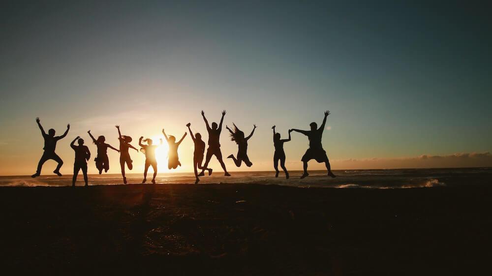People jumping on beach in front of sunset