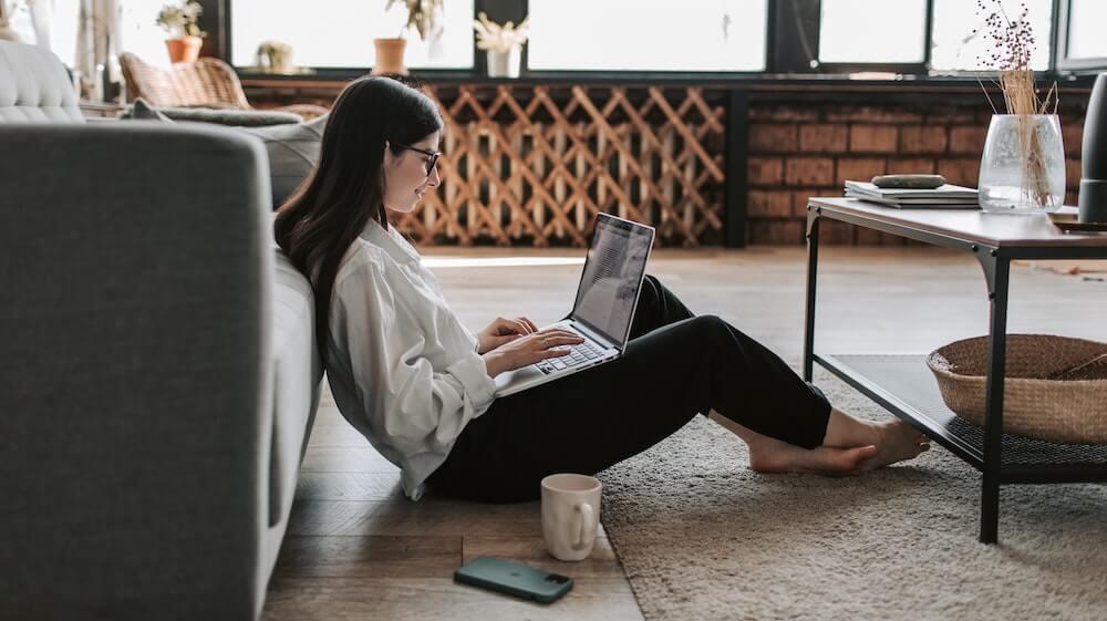 Woman working from home sitting on floor with laptop