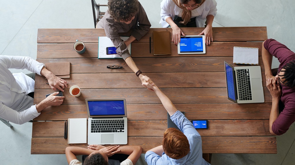 People sitting around a meeting table, two are shaking hands