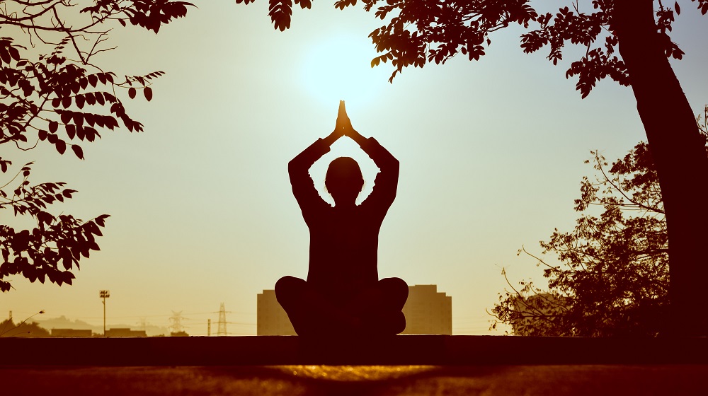 Person meditating under trees with city in the distance