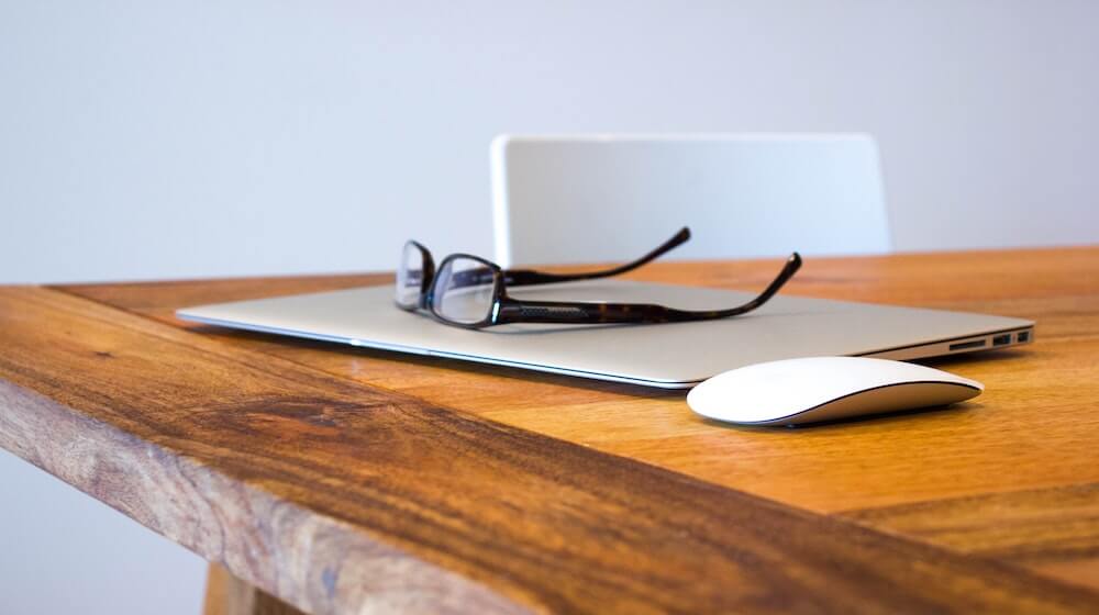 Closed laptop on desk with reading glasses on top-2