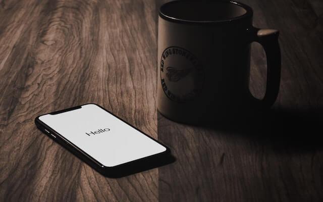 Mobile phone showing hello on screen next to coffee mug-2