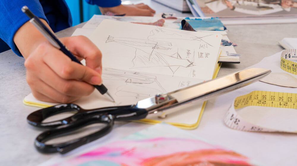 person designing clothes in notebook