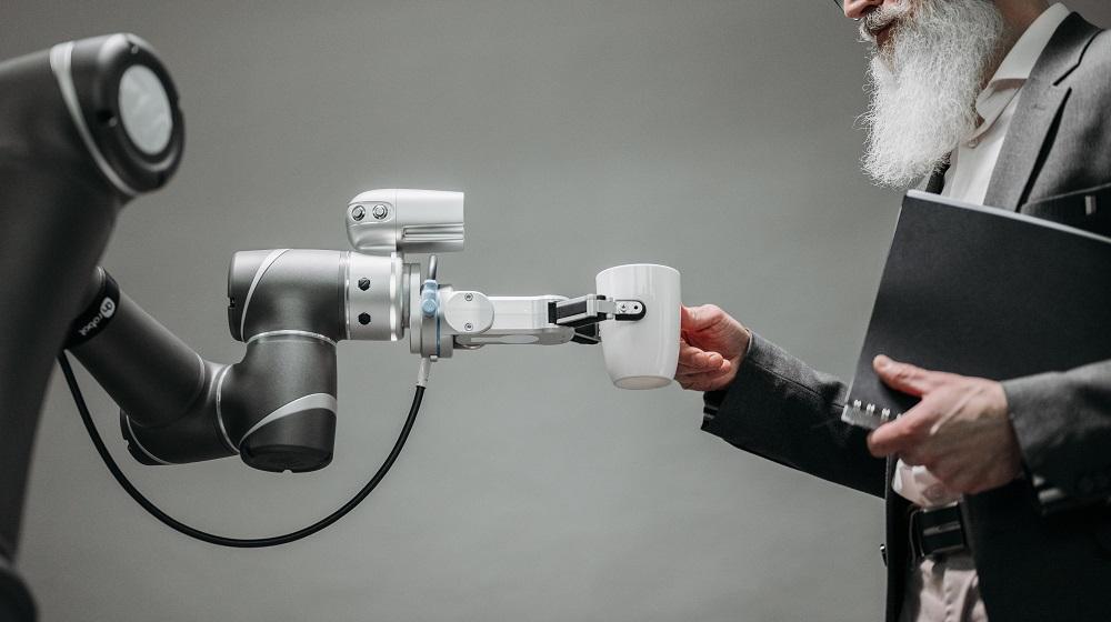 Robot passing a mug to a bearded man holding a folder