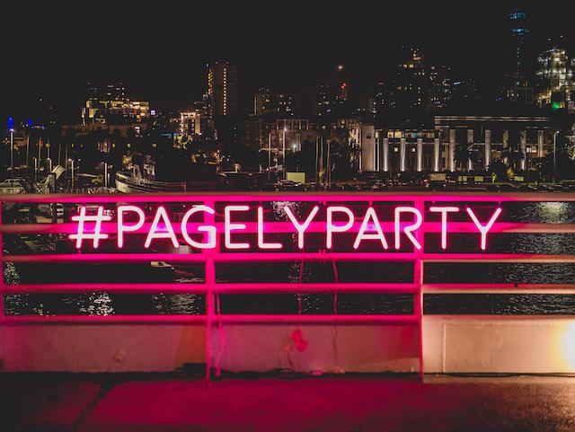 Neon pink Pagely sign lit up at night with San Diego cityscape in background