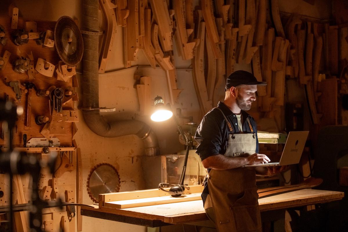 man holding an open laptop in a dark workshop