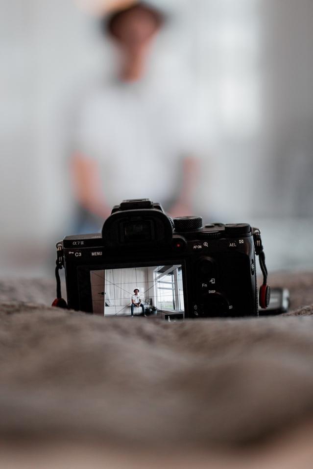 Close-up of DSLR camera facing a male model posing in a white t-shirt and hat