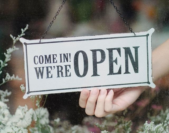 A person holding a window sign that reads, &quot;Come in! We're open&quot;