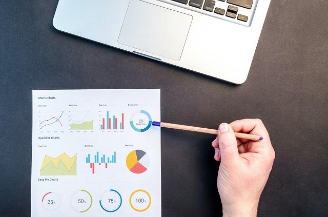 A laptop and data chart resting on a desk with someone reviewing the data chart.