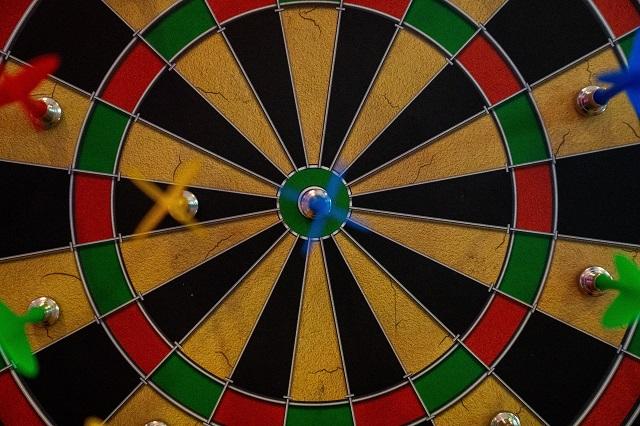 Close up picture of a dart board with darts scattered about.