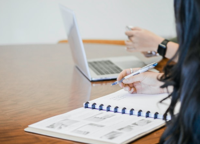 Two people reviewing a notebook and laptop on a long table