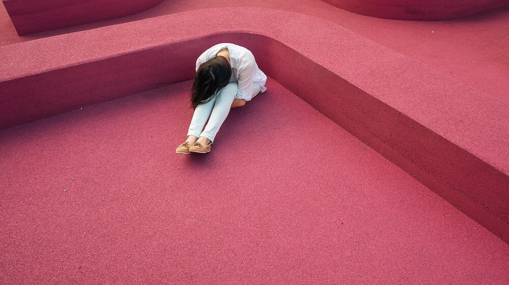 Woman hunched over with head down sitting on red background
