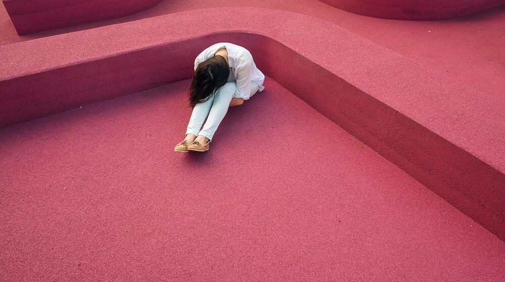 Woman hunched over with head down sitting on red background