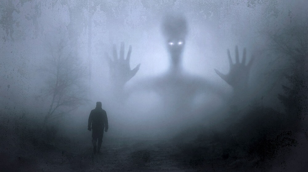 Person walking into gloomy forest with ethereal image of an alien in the background