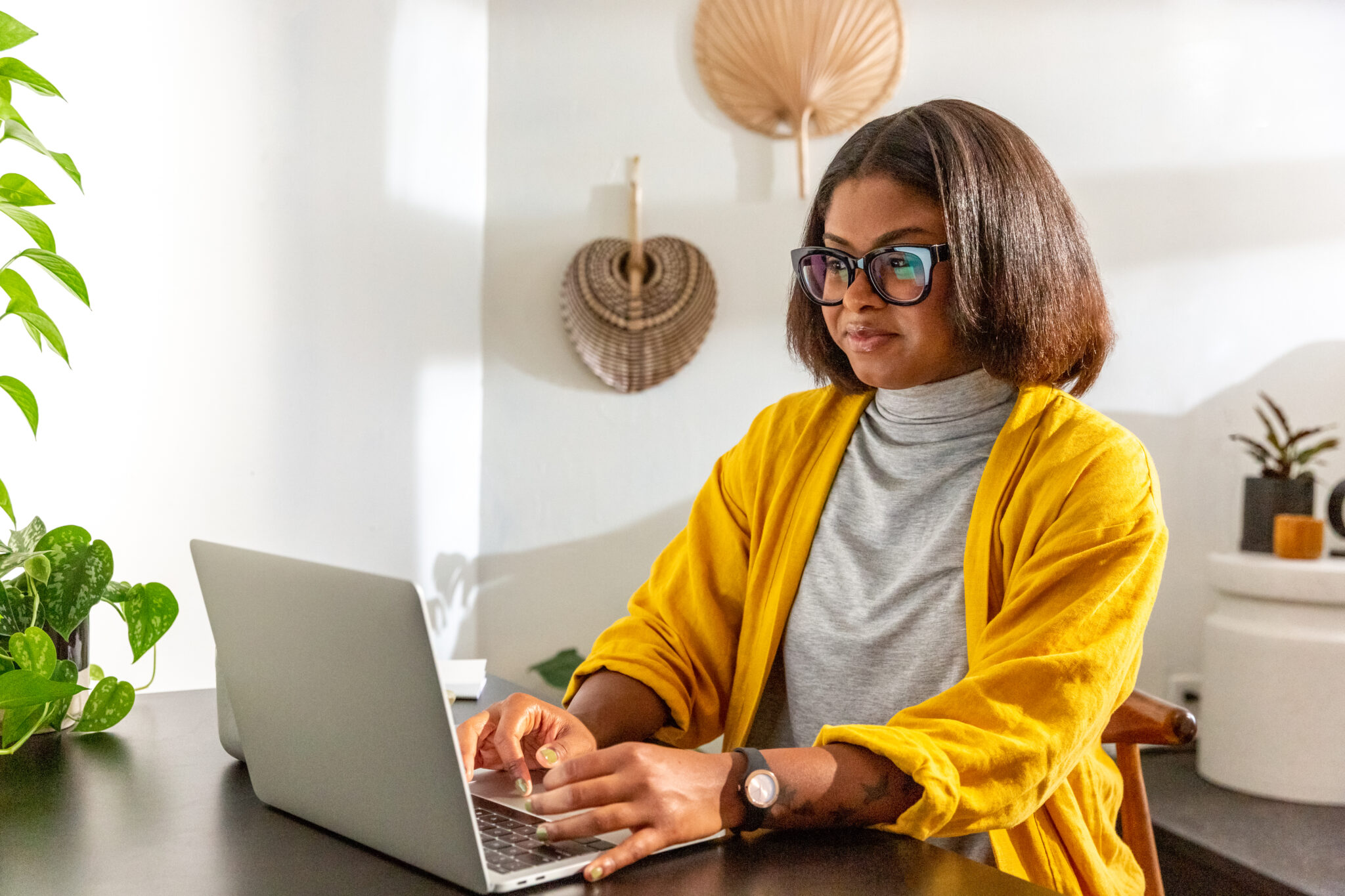 Woman in yellow sweater at desk looking at laptop