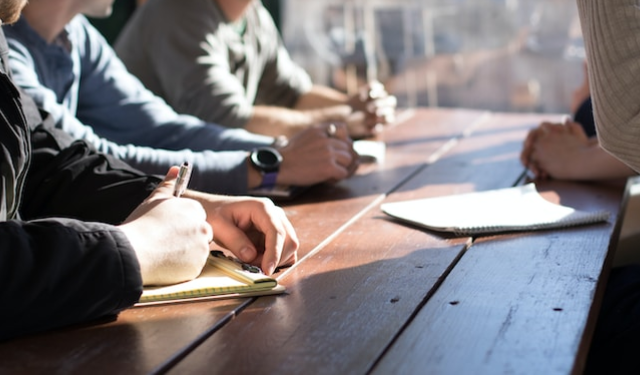People sitting around a long wooden table taking notes on notepads