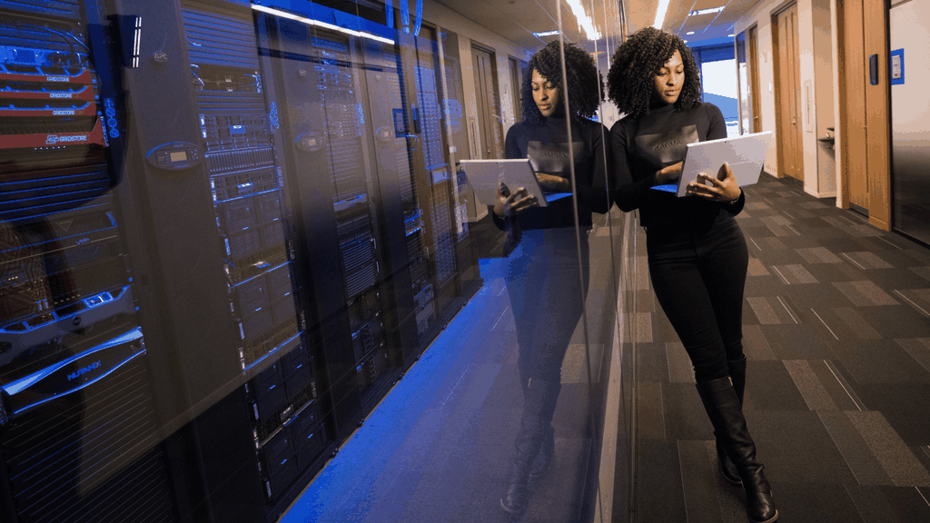 Woman looking at a laptop, standing in front of server room