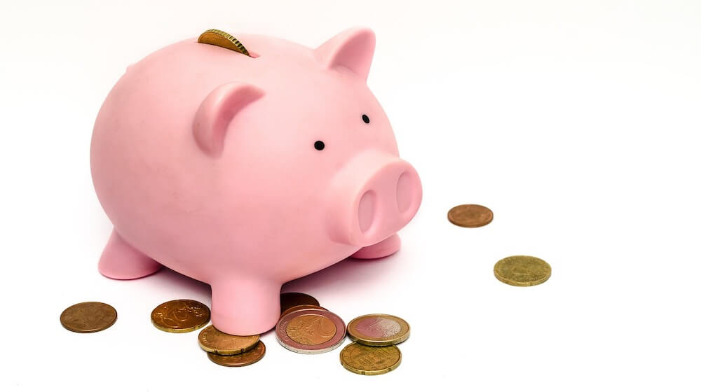 Pink piggy bank standing over scattered coins(1)