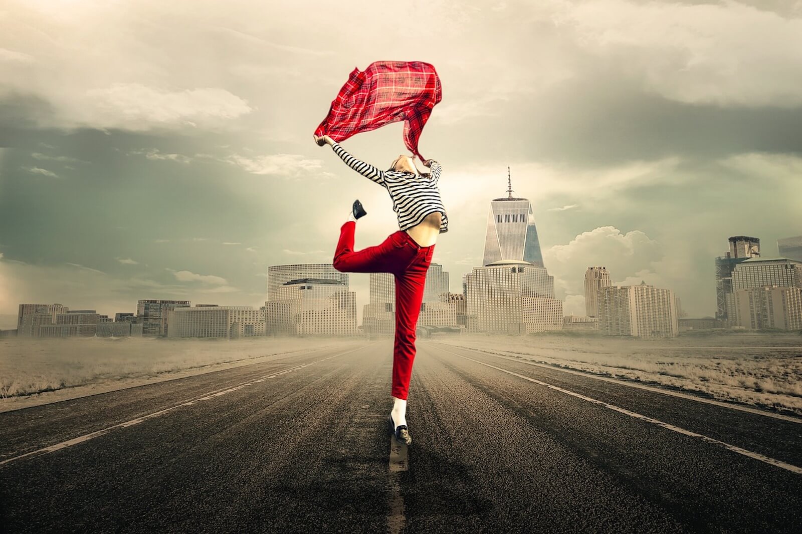 Woman in red pants posing on one leg with billowing red scarf in a cityscape background(1)