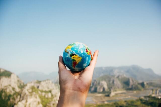 Person holding a ball that looks like the world against an outdoor setting