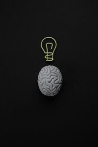 Figure of a brain on black background with lightbulb on top