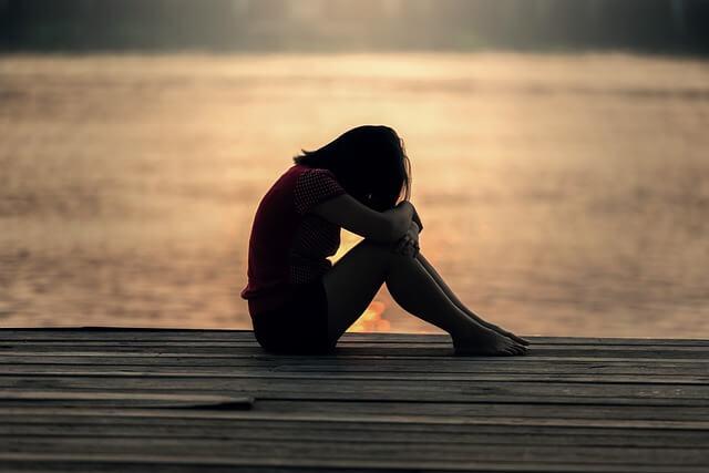 Woman sitting with her head in her lap on an outdoor deck by the lake.