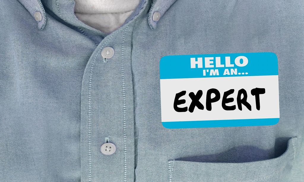 Closeup shot of a chambray shirt with a name tag that reads "Hello, I'm an expert"