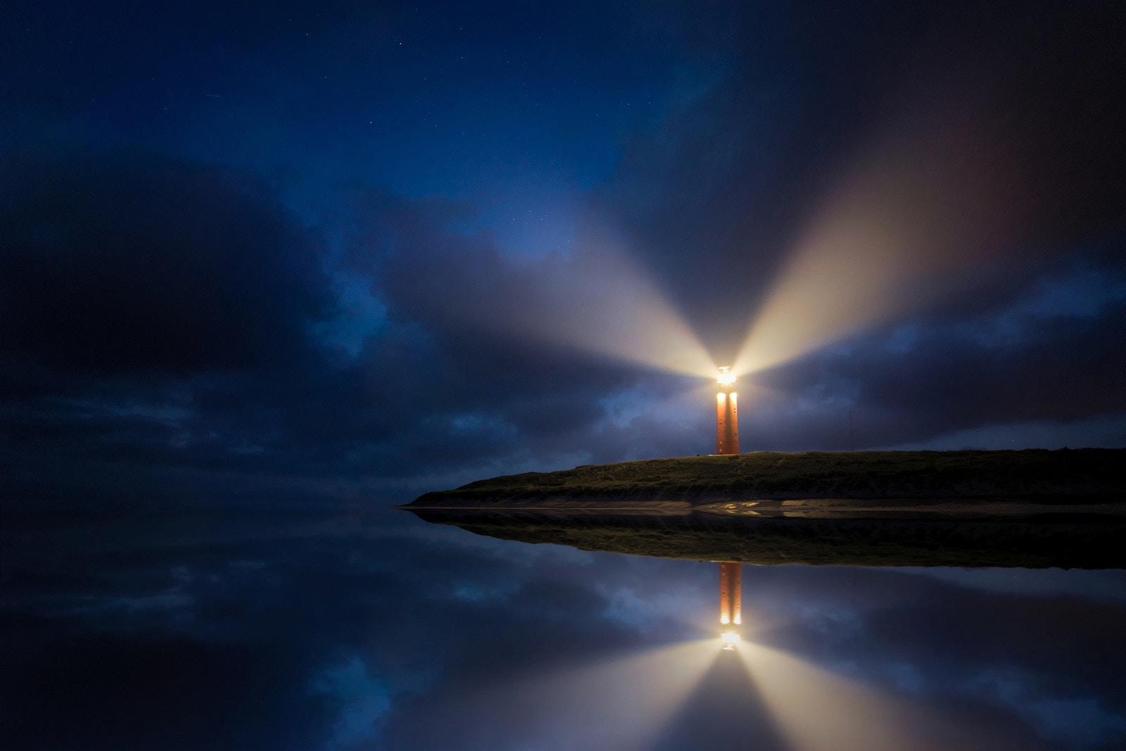 A light house on a hill with a reflection of clouds in the water