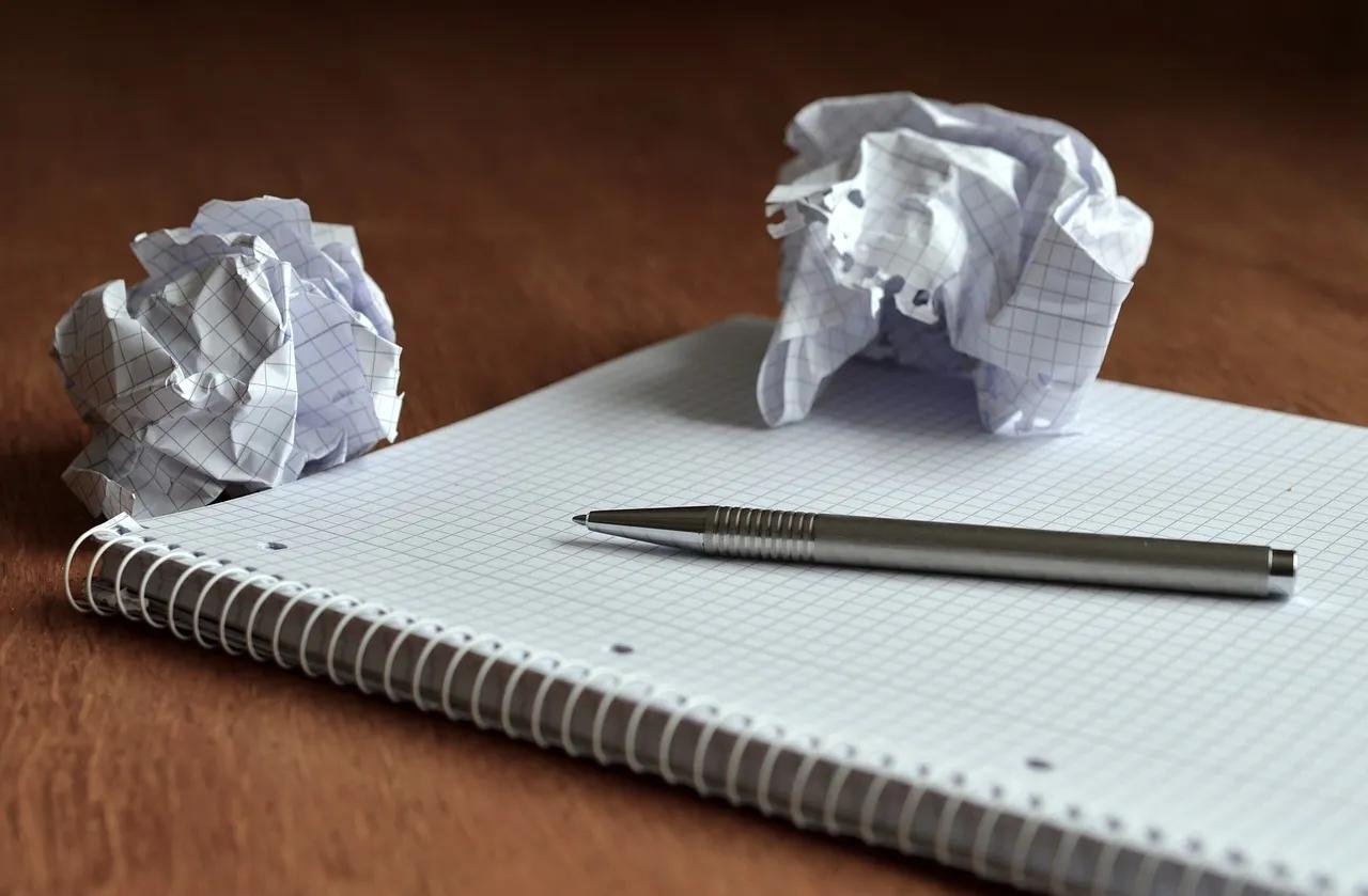 Crumpled Paper Sits atop a Desk with a Notebook and Pen
