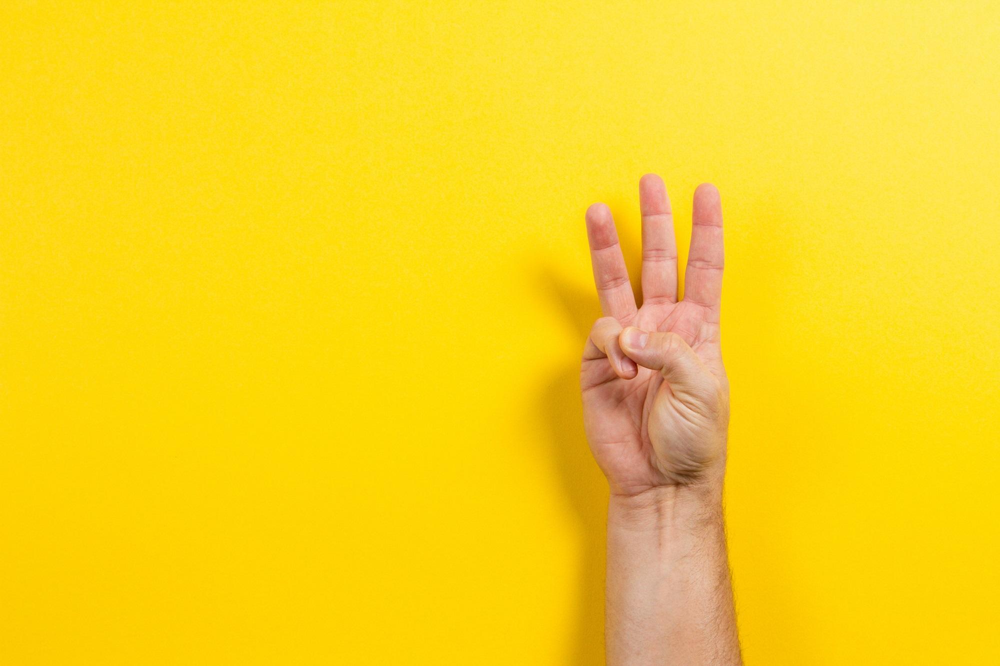 A human hand showing the &quot;OK&quot; sign against a bright yellow background.