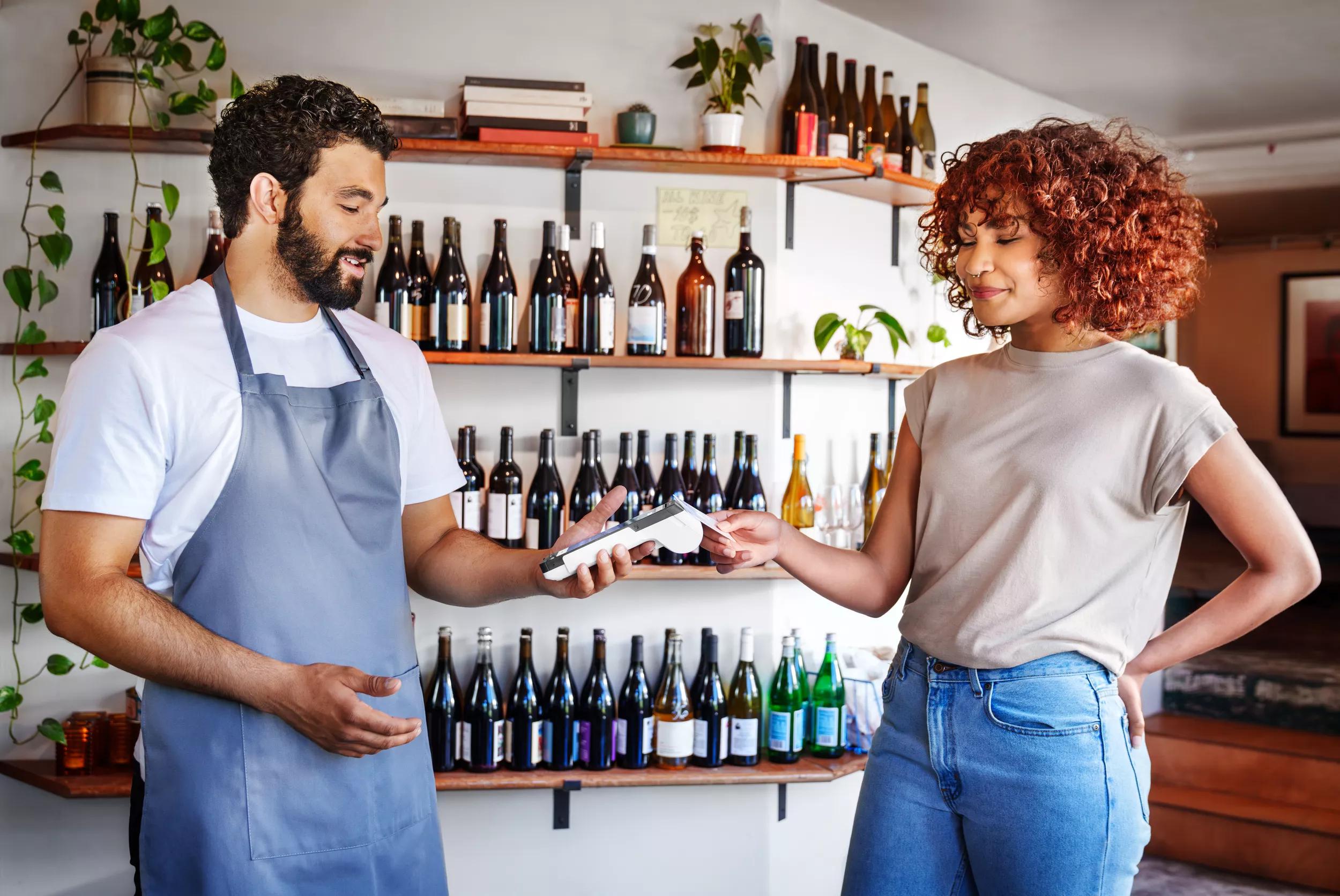 A wine store business owner is accepting payments with a compact mobile point of sale from a customer