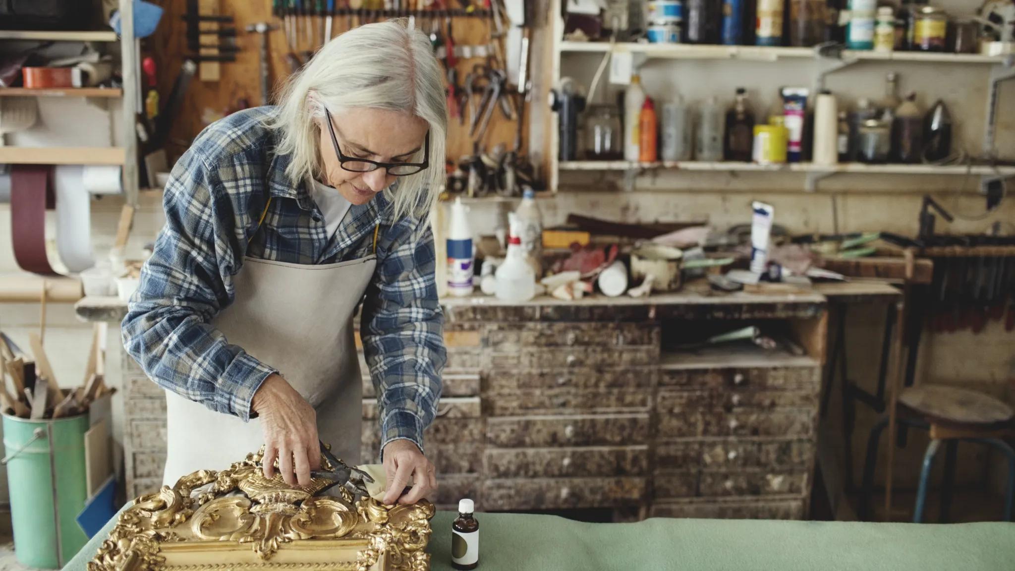 Woman working on an ornate golden picture frame.