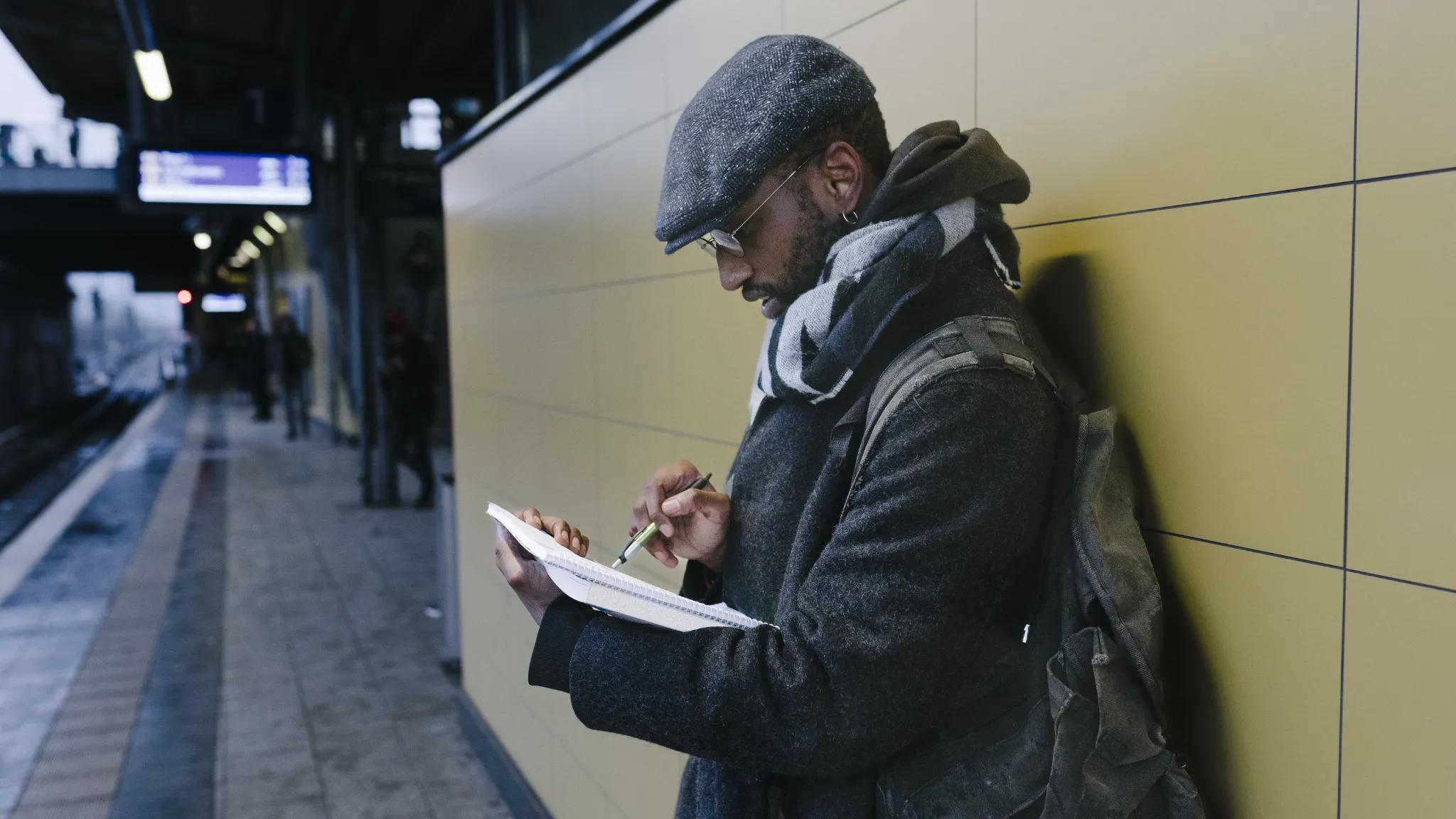 Man reviewing notebook with pen in hand at a train station.