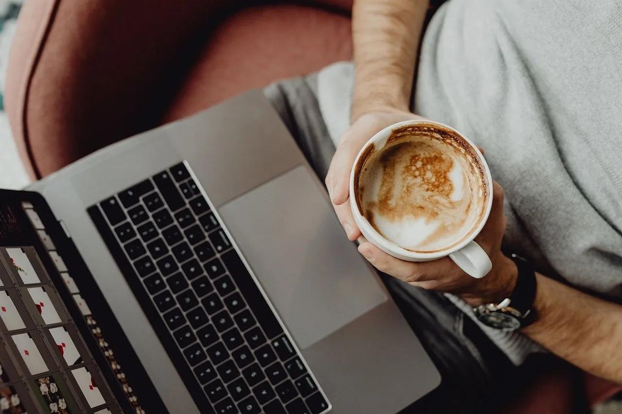 An Overhead Shot of a Person Holding a Coffee Cup Seated in Front of a Laptop