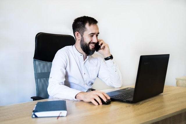 Catalog Management Smiling Man on Phone Working with Laptop