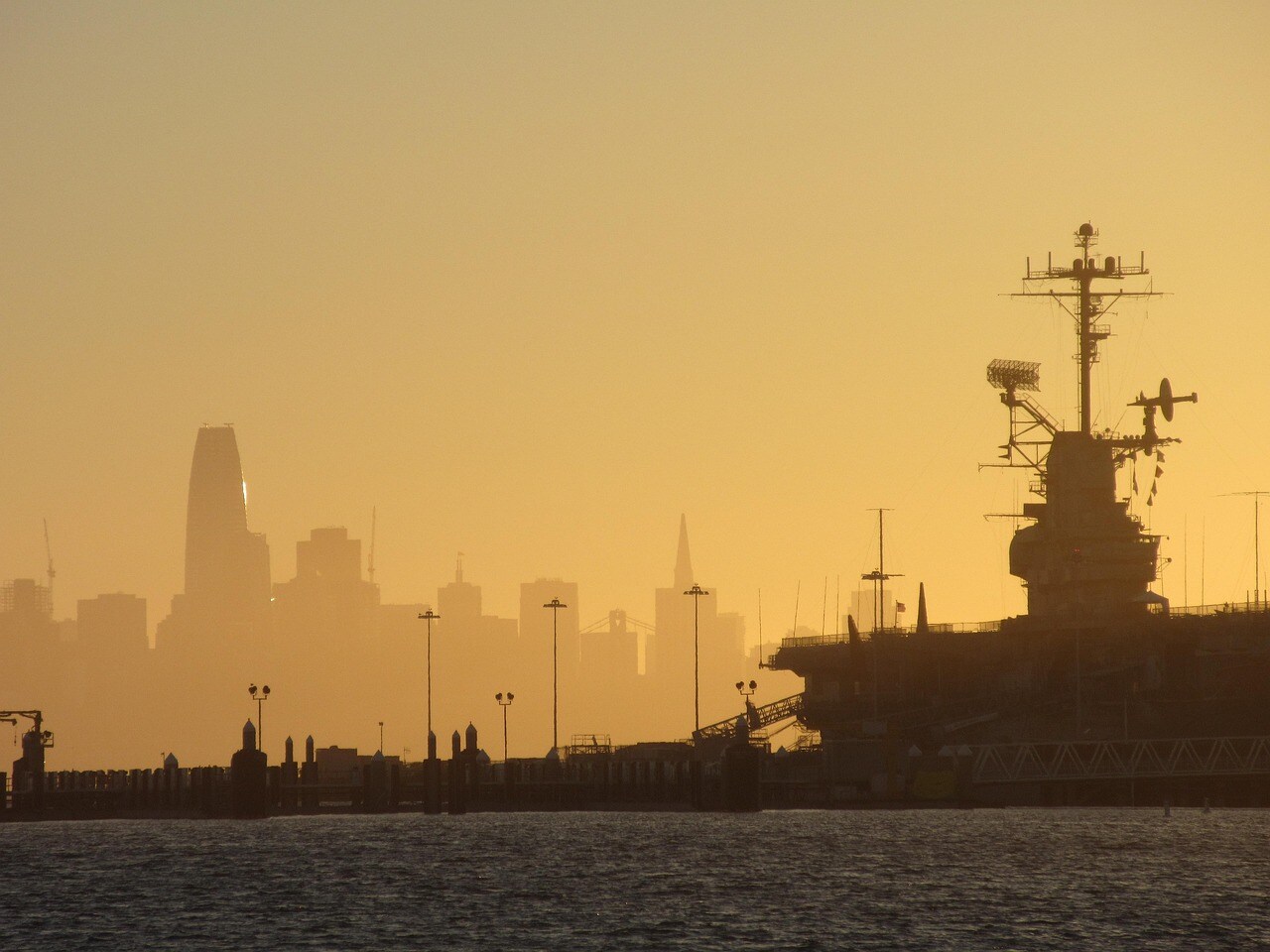 A Landscape Photo Featuring the Alameda Skyline with a Docked Warship in the Foreground