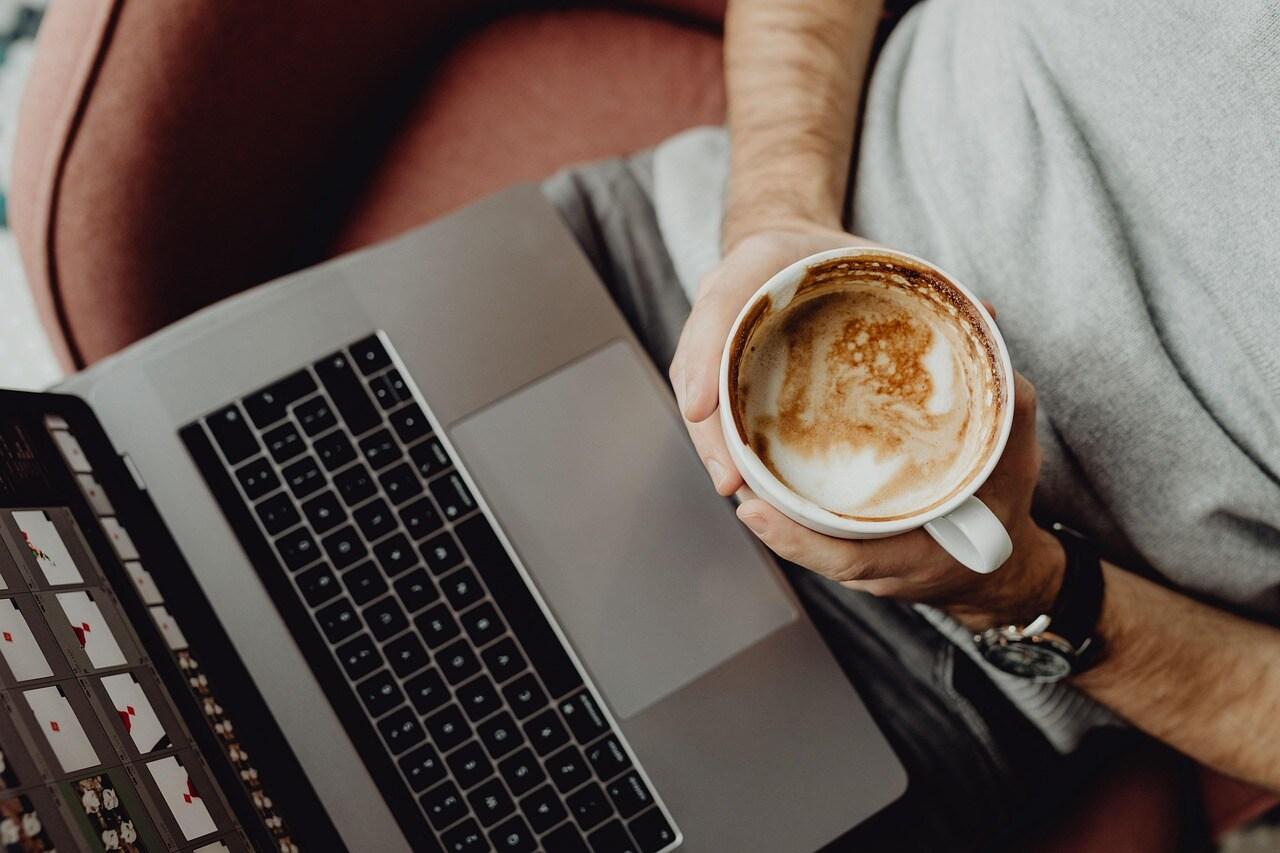 An Overhead Shot of a Person Holding Coffee in Front of a Laptop