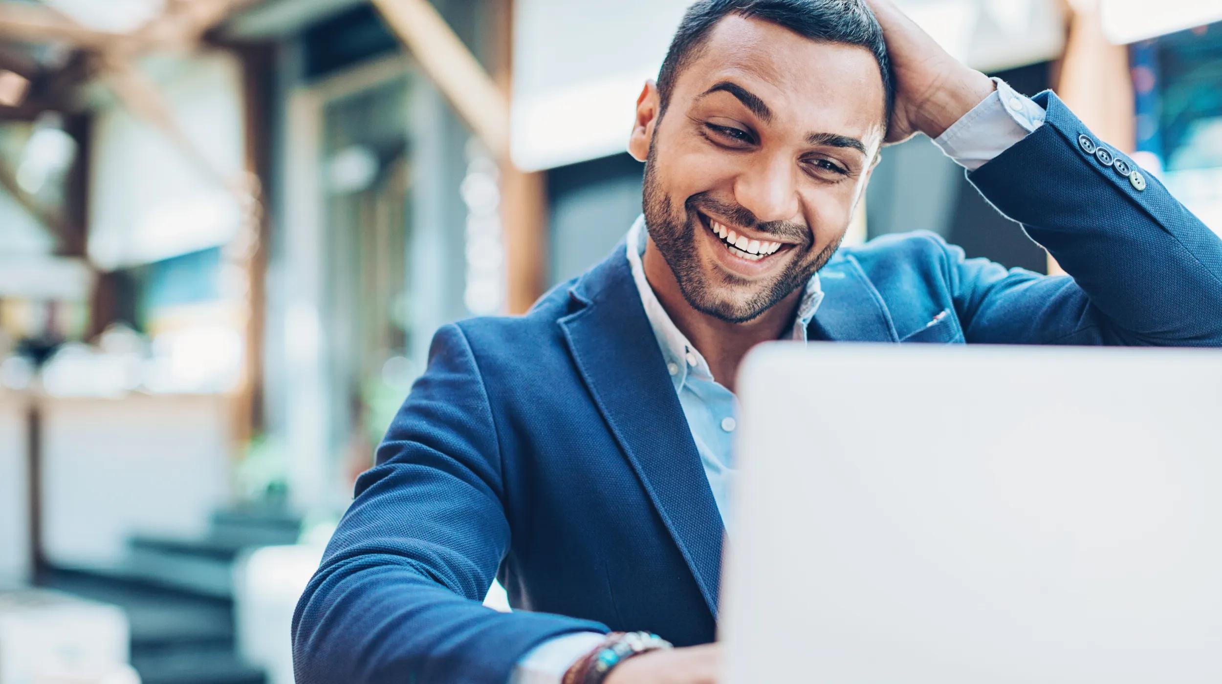 Smiling man in a blue blazer working on a laptop in a bright, modern office, representing a successful entrepreneur starting an LLC in Nevada.
