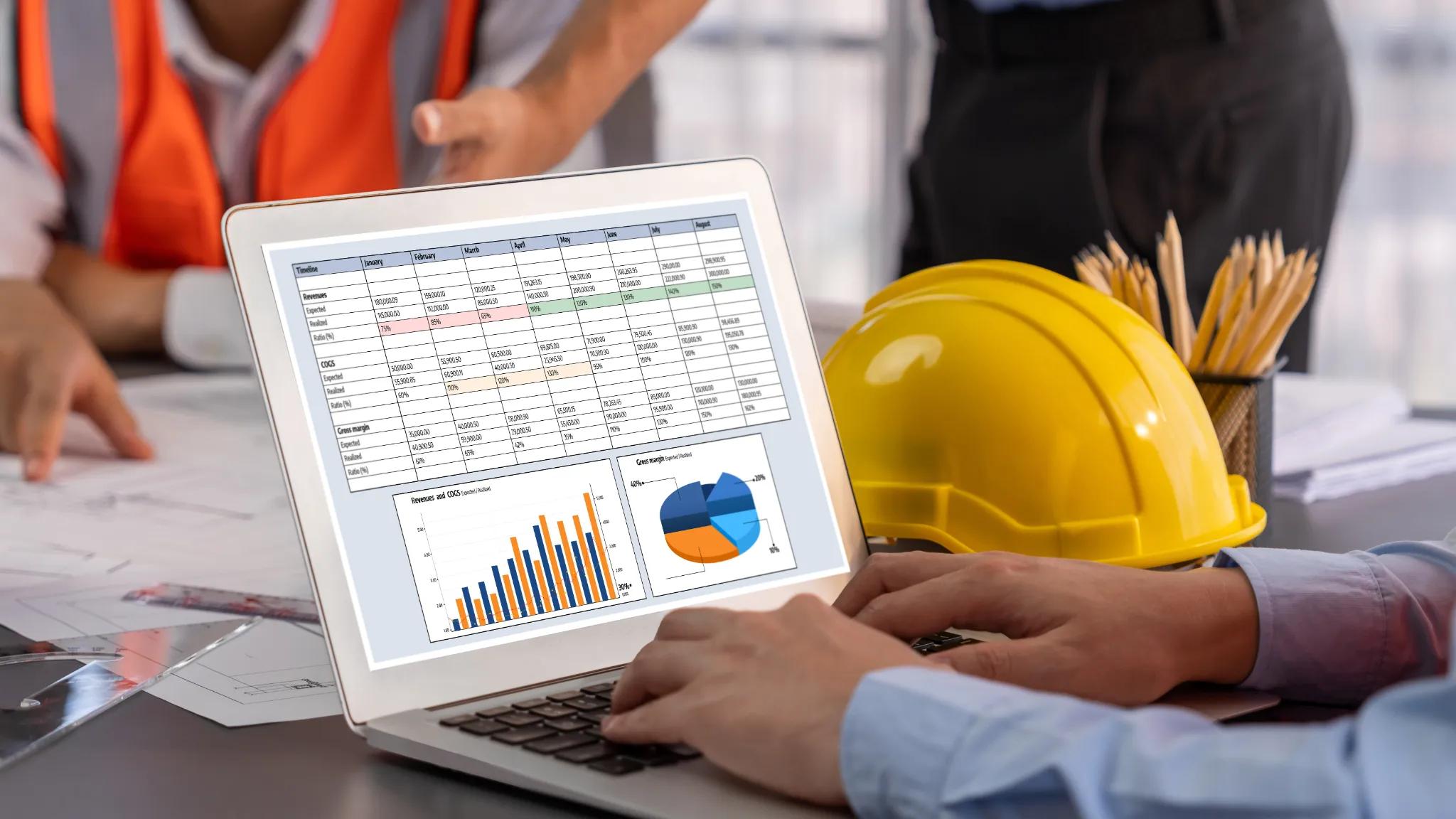 A laptop showing business metrics and charts, resting on a desk next to a hard hat.